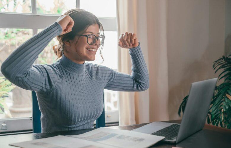 One happy euphoric young woman winning something on the laptop at home on desk.